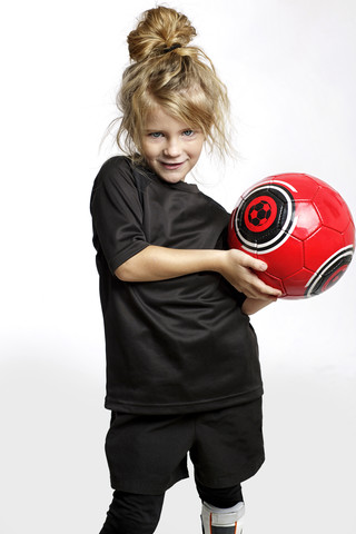 Portrait of blond girl with red soccer ball wearing football sportswear in front of white background stock photo