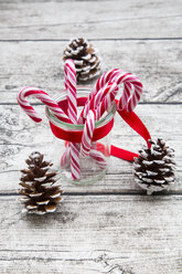 Glas mit Zuckerstangen und Tannenzapfen auf Holz - LVF002396