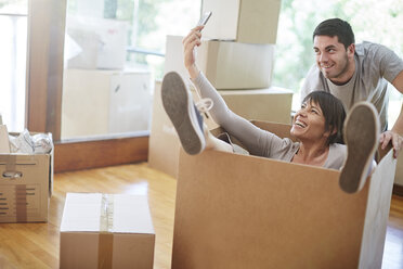 Playful couple moving house sitting in a box taking a selfie - ZEF002855