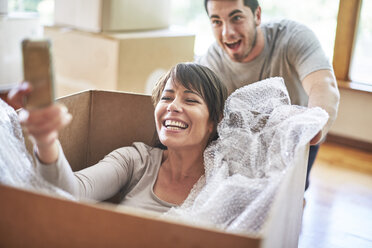 Playful couple moving house sitting in a box taking a selfie - ZEF002856