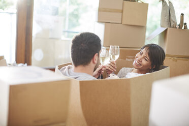 Couple moving house sitting in a box and clinking wine glasses - ZEF002857