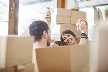 Couple moving house sitting in a box with key and wine glasses - ZEF002858