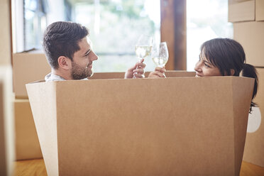 Couple moving house sitting in a box and clinking wine glasses - ZEF002859