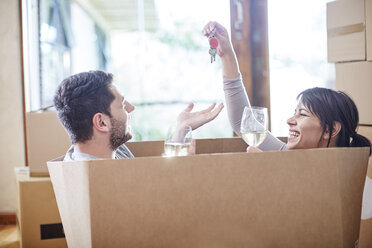 Couple moving house sitting in a box with key and wine glasses - ZEF002860