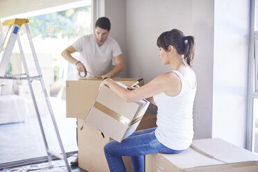 Couple moving house, woman writing on box - ZEF002879