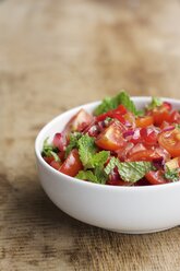 Schale mit Tomaten- und Granatapfelsalat, garniert mit Minzblättern auf Holz - HAWF000523
