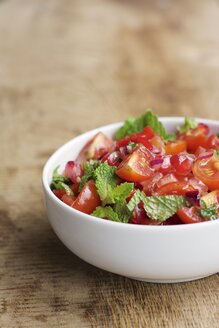 Schale mit Tomaten- und Granatapfelsalat, garniert mit Minzblättern auf Holz - HAWF000523