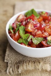 Schale mit Tomaten- und Granatapfelsalat, garniert mit Minzblättern auf Jute und Holz - HAWF000524