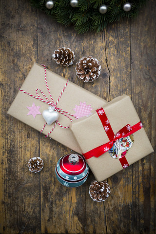 Eingepackte Weihnachtsgeschenke, Weihnachtskugeln und Tannenzapfen auf dunklem Holz, lizenzfreies Stockfoto