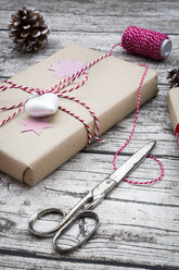 Eingepackte Weihnachtsgeschenke, Schere, Schleife und Tannenzapfen auf Holz - LVF002403