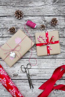 Eingepackte Weihnachtsgeschenke, Tannenzapfen, Schleife und Schere auf Holz - LVF002402