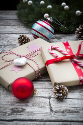 Eingepackte Weihnachtsgeschenke, Weihnachtskugeln und Tannenzapfen auf Holz - LVF002401