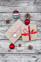 Eingepackte Weihnachtsgeschenke, Weihnachtskugeln und Tannenzapfen auf Holz - LVF002400