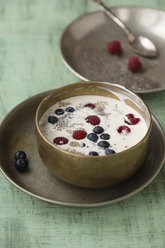 Metal bowl of vanilla yoghurt with chia, Salvia hispanica, blueberries and raspberries on green wood - MYF000732