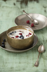 Metal bowl of vanilla yoghurt with chia, Salvia hispanica, blueberries and raspberries on green wood - MYF000733