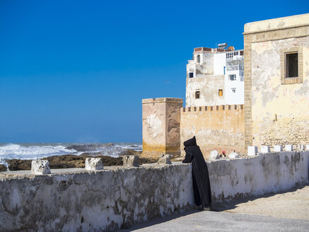Marokko, Essaouira, Berber in schwarzer Djellaba an der Hafenmauer - AM003397
