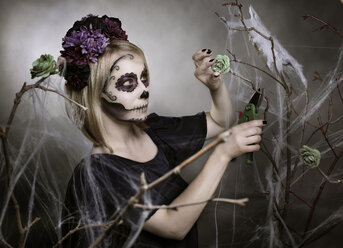 Frau mit Zuckerschädel-Makeup schneidet Blüte mit Gartenschere - NIF000026