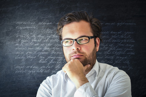 Porträt eines nachdenklichen Mannes mit Vollbart und Brille vor einem dunklen Hintergrund mit Schriftzeichen, lizenzfreies Stockfoto