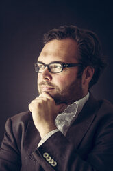 Portrait of pensive man with full beard wearing glasses in front of dark background - PUF000353