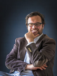 Portrait of smiling man with full beard wearing glasses in front of dark background - PUF000354