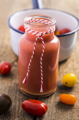 Glass of tomato smoothie and different mini tomatoes on wood - ODF000909