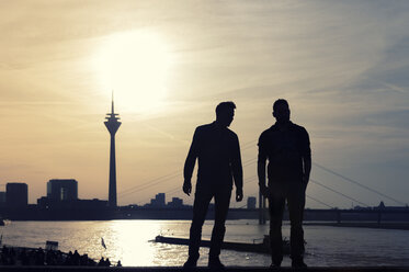 Deutschland, Nordrhein-Westfalen, Düsseldorf, zwei Männer schauen zum Rheinturm und zum Rhein bei Sonnenuntergang - FRF000140