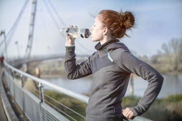 Junge Frau trinkt nach dem Joggen Wasser aus einer Flasche - SEGF000070