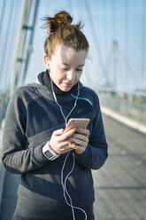 Portrait of young female jogger with heart rate monitor, earphones and smartphone hearing music - SEGF000071