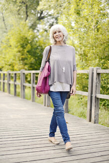 Porträt einer lächelnden weißhaarigen älteren Frau, die auf einer Holzpromenade spazieren geht - VRF000135