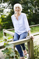 Porträt einer lächelnden weißhaarigen älteren Frau, die auf einem Holzgeländer sitzt - VRF000130
