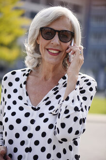 Porträt einer lächelnden älteren Frau mit Sonnenbrille, die mit einem Smartphone telefoniert - VRF000129