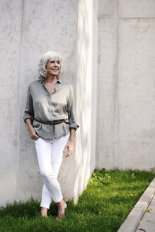 Smiling white haired senior woman leaning against concrete wall - VRF000122