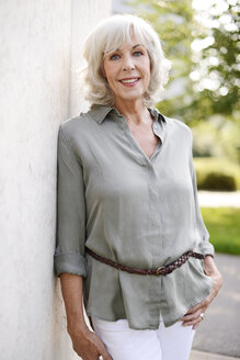 Portrait of smiling white haired senior woman leaning against concrete wall - VRF000120