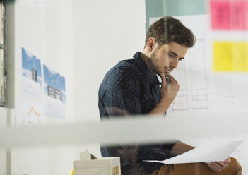 Young man in office reviewing documents - UUF002773