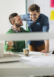 Zwei lächelnde junge Männer in einem Büro mit einem Architekturmodell - UUF002787