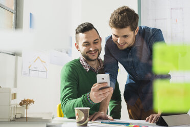 Two smiling young men in office looking at cell phone - UUF002788