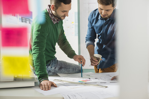 Zwei junge Männer im Büro besprechen einen Bauplan, lizenzfreies Stockfoto