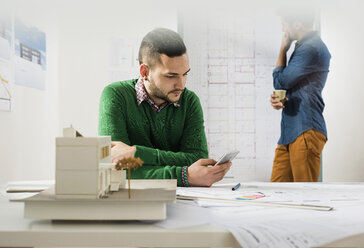 Zwei junge Architekten im Büro mit Handy und Bauplan - UUF002796