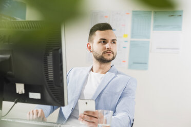 Young businessman in office with computer and cell phone - UUF002827