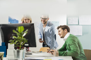 Drei junge Leute im Büro schauen auf einen Computerbildschirm - UUF002833