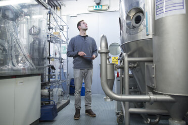 Young man with digital tablet in technical room looking up - SGF001194