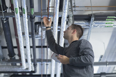 Young man with digital tablet in technical room checking pipe - SGF001204