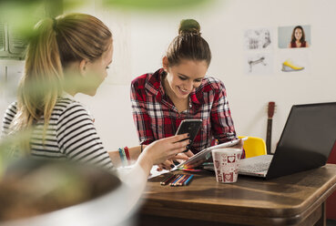 Zwei Freundinnen mit Smartphone, Laptop und digitalem Tablet zu Hause - UUF002751