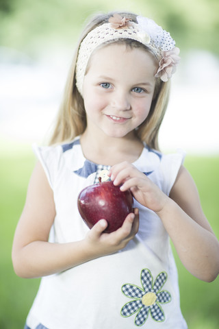 Porträt eines lächelnden kleinen Mädchens mit Haarband, das einen roten Apfel hält, lizenzfreies Stockfoto