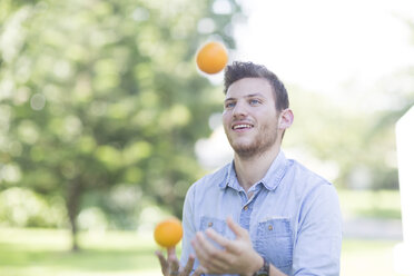 Young man juggling with oranges outdoors - ZEF003499