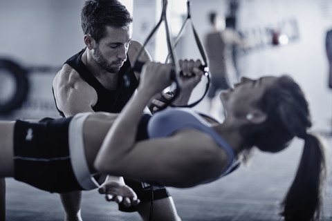 Fitnesstrainer hält den Takt mit einer Frau, die Klimmzüge macht, lizenzfreies Stockfoto