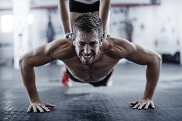 Man doing push-ups with woman kneeling on his back stock photo