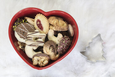 Heart-shaped bowl of different Christmas Cookies and a cookie cutter on an angel wing - SARF001143