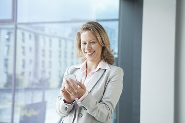 Lächelnde Geschäftsfrau, die im Büro ein Mobiltelefon benutzt - RBF002114