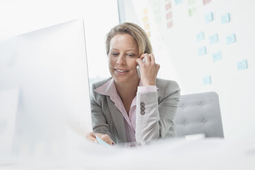 Smiling businesswoman on the phone in office - RBF002143